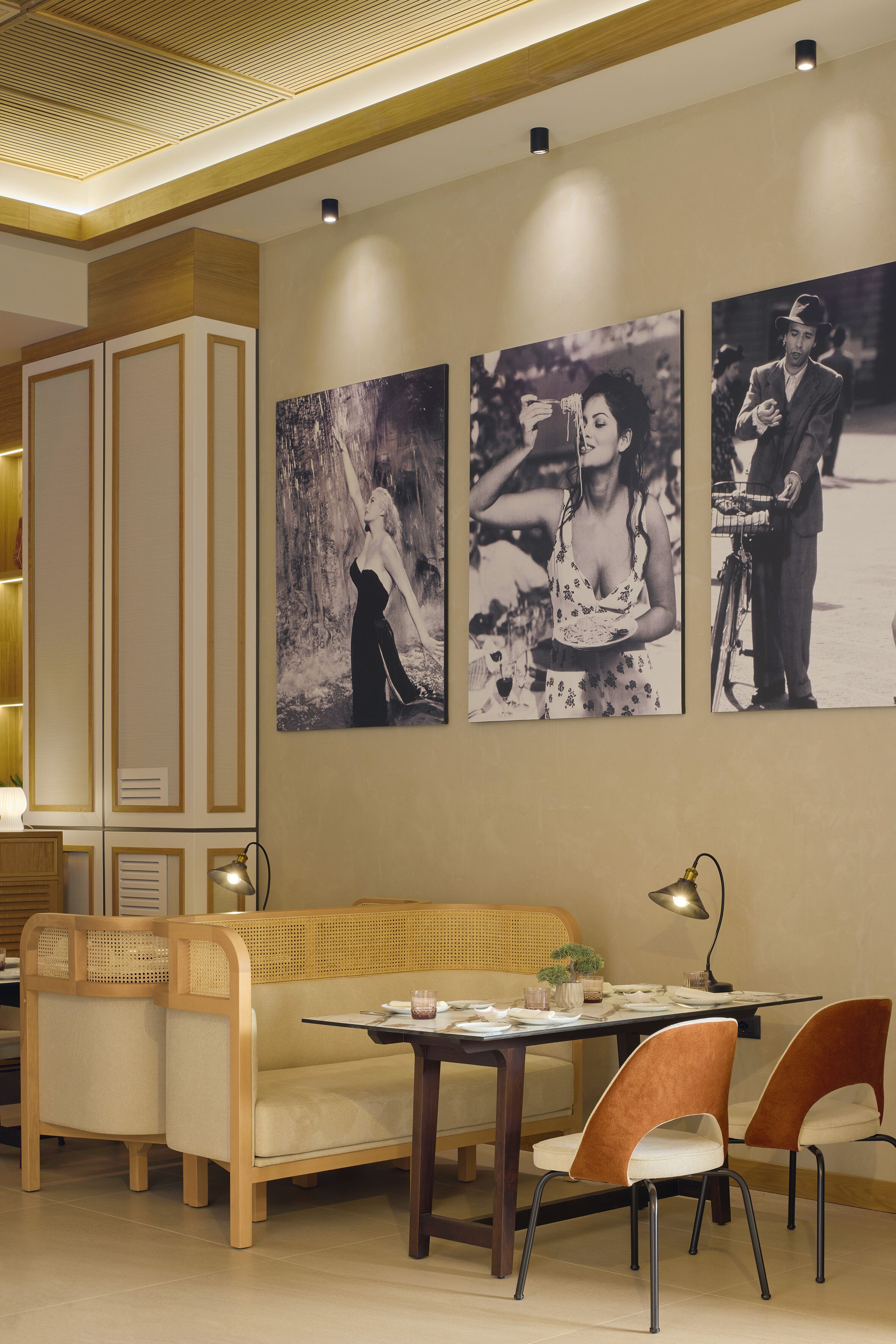 A dining area with a wooden table, two chairs, a sofa, and wall-mounted artwork.