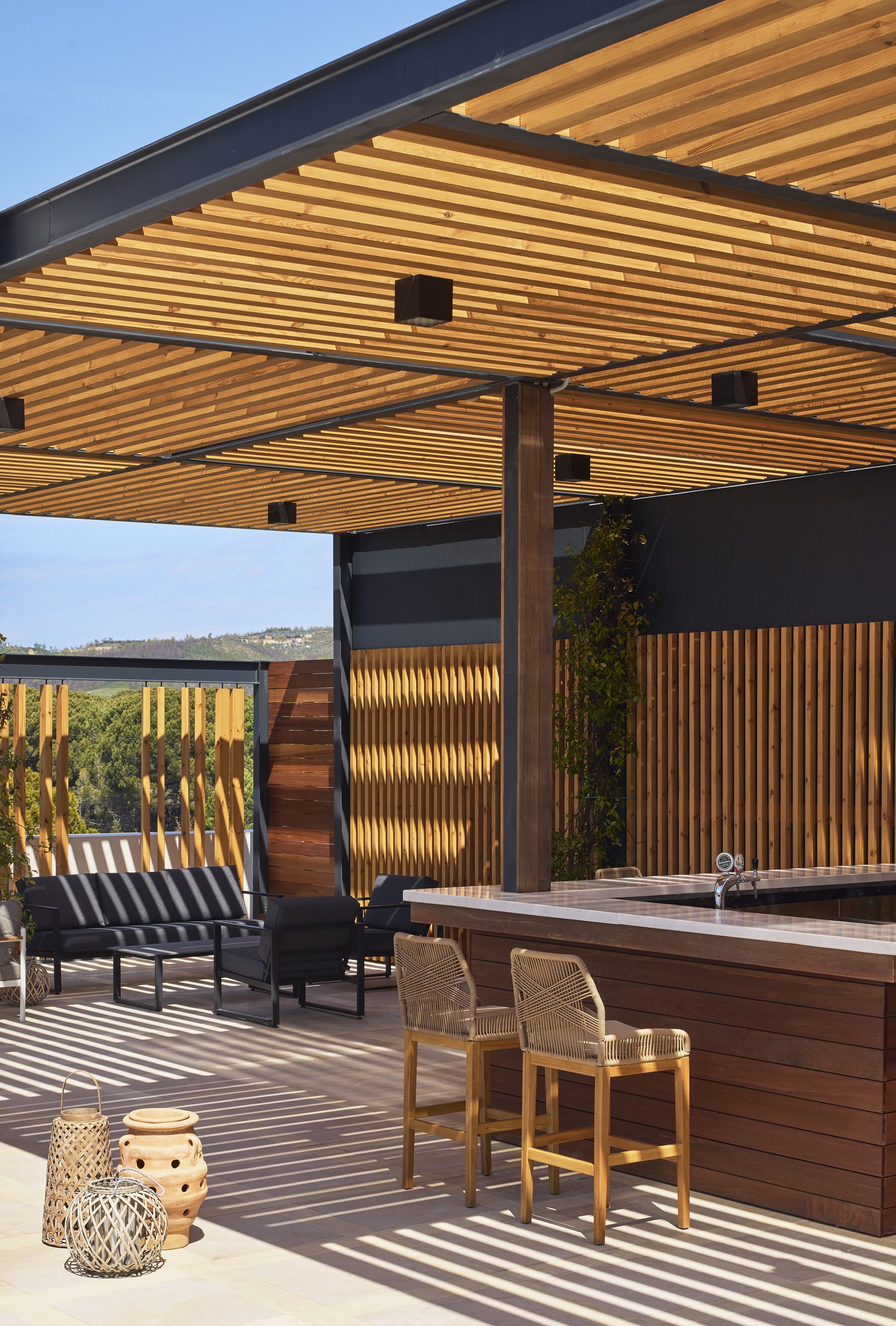 Une terrasse extérieure dotée d’une pergola en bois, d’un espace salon et d’un bar.