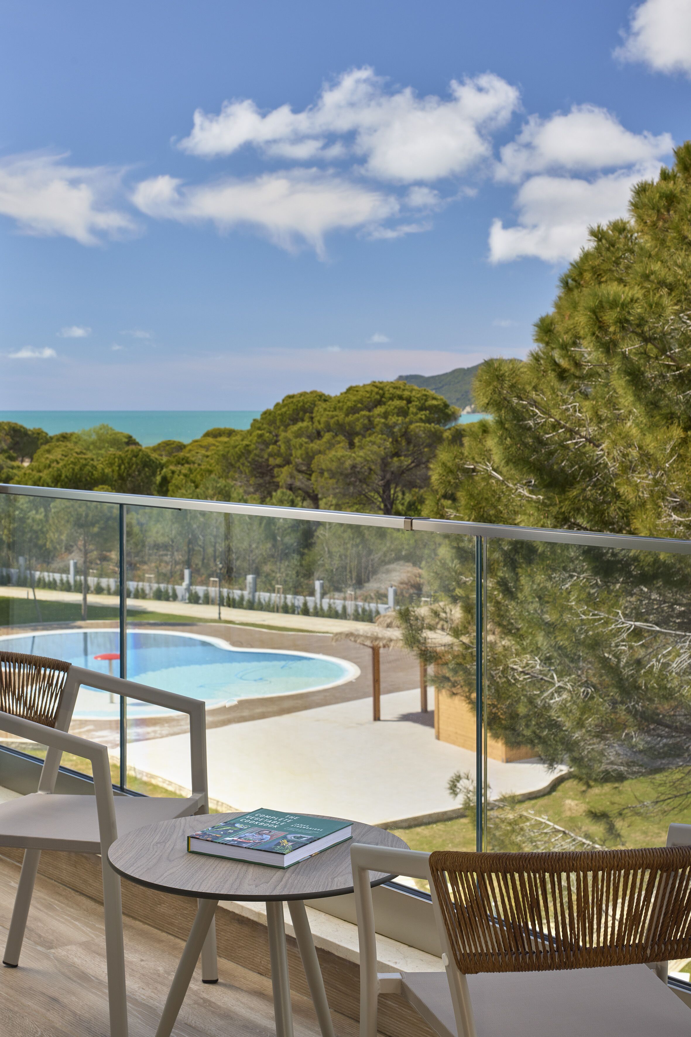 A balcony with a view of a swimming pool, outdoor seating, and a book on a table.