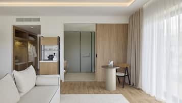 Une chambre d’hôtel moderne, dotée d’un canapé, d’une table ronde, d’une chaise, d’une armoire et offrant une vue sur l’extérieur à travers une fenêtre ornée de rideaux légers.