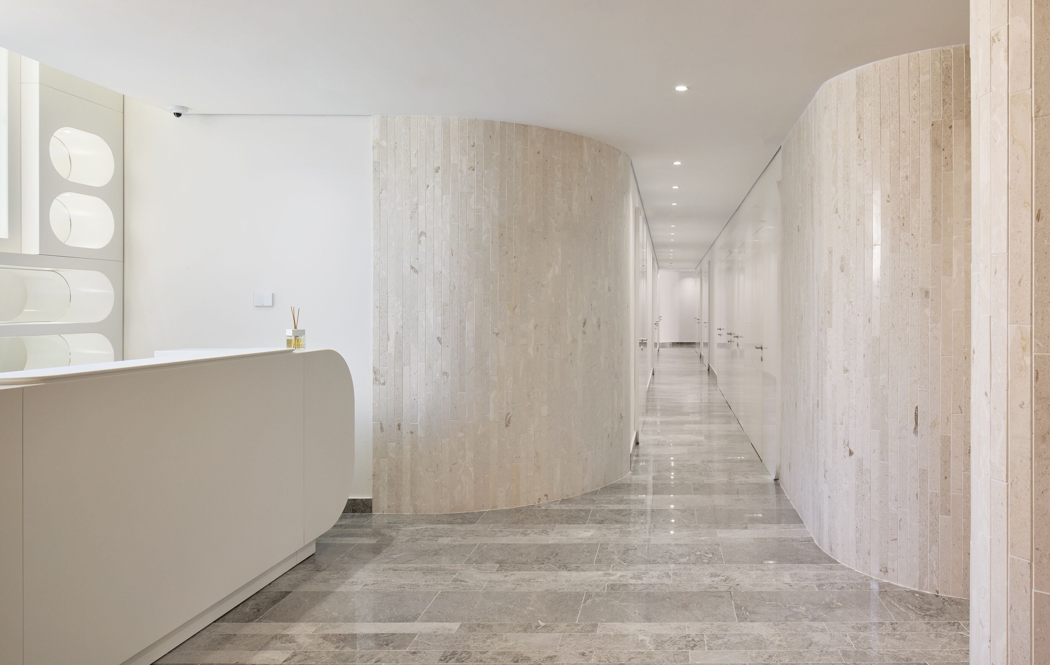 Um corredor moderno com uma recepção em balcão curvo, paredes de mármore e chão de azulejos.