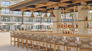 A bar area with wicker chairs, a bar counter with bottles, and a view of the pool and building in the background. - Melia Durres Albania (Ishëm)
