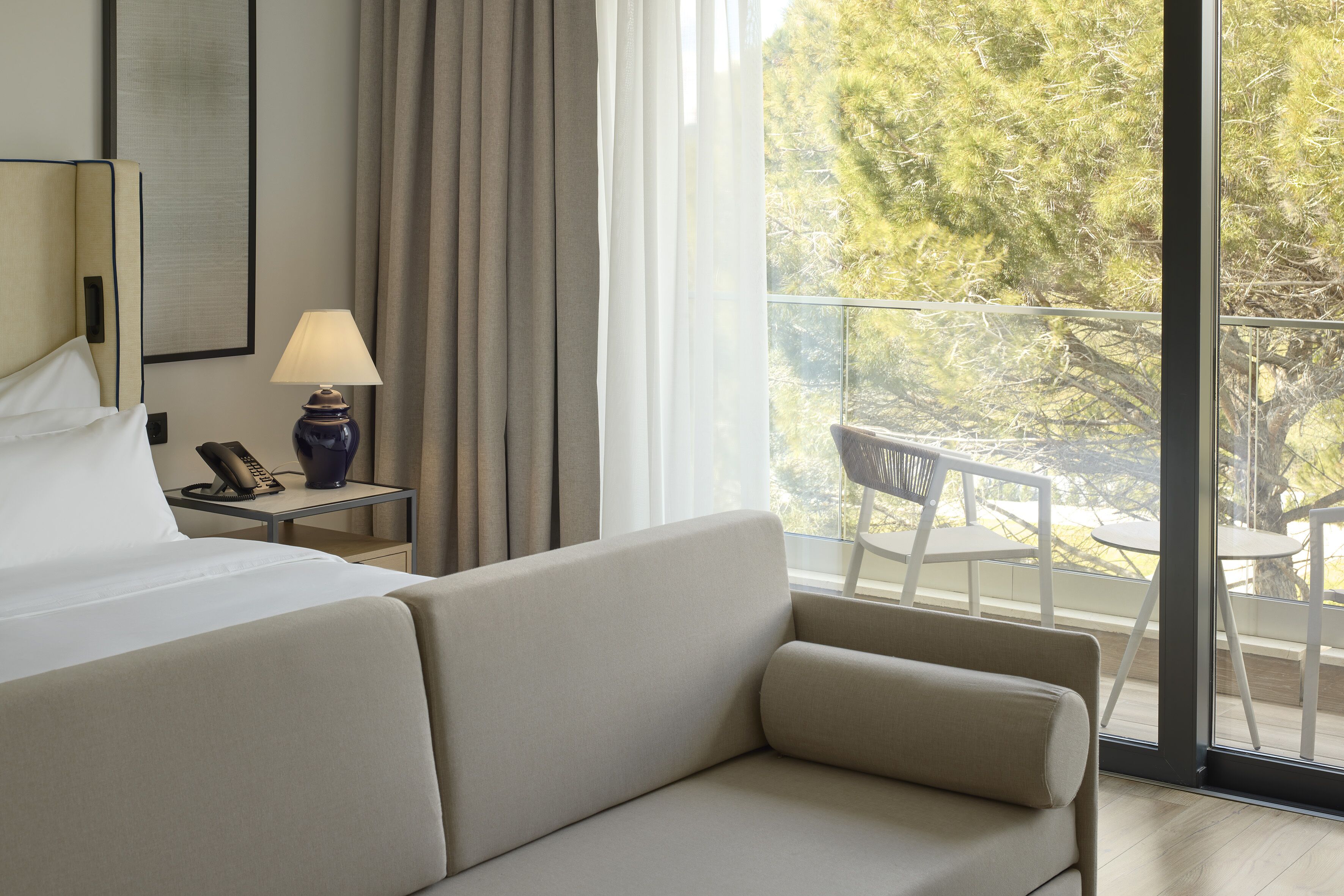 Une chambre d’hôtel comprenant un lit, un canapé, une lampe, un téléphone et donnant sur un balcon aménagé avec du mobilier d’extérieur.