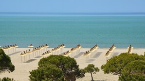 A beach with rows of umbrellas and chairs, trees in the foreground, and the sea in the background. - Melia Durres Albania (Ishëm)