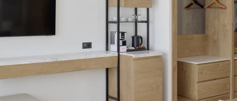 Habitación moderna con escritorio integrado, televisión de pantalla plana, cafetera y armario de madera con espacio para colgar.