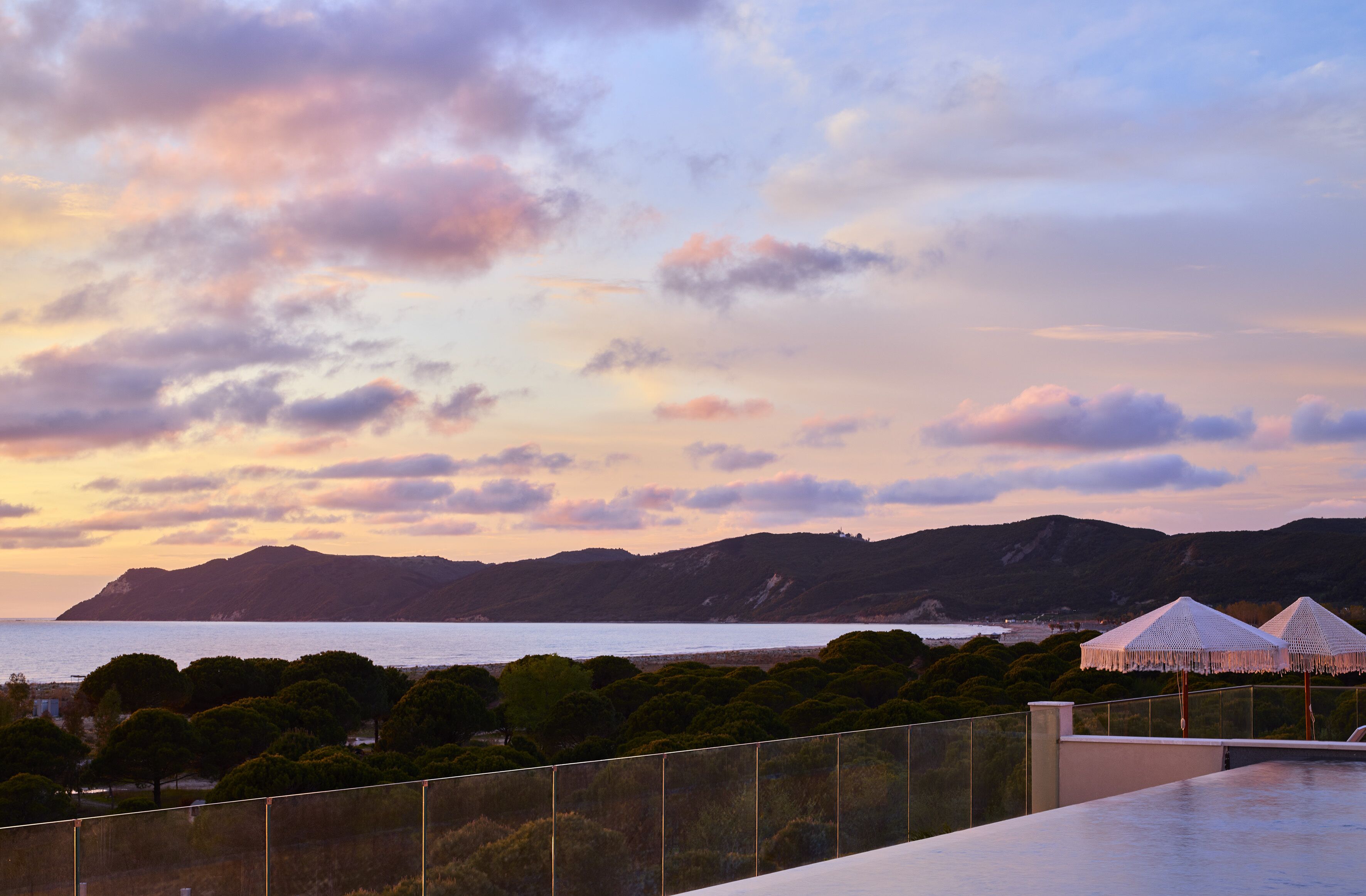 A coastal view with a beach, mountains, and a fenced area with umbrellas.