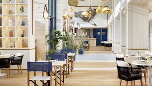 A modern restaurant interior with wooden tables and chairs, hanging pendant lights, and potted plants. - Melia Durres Albania (Ishëm)