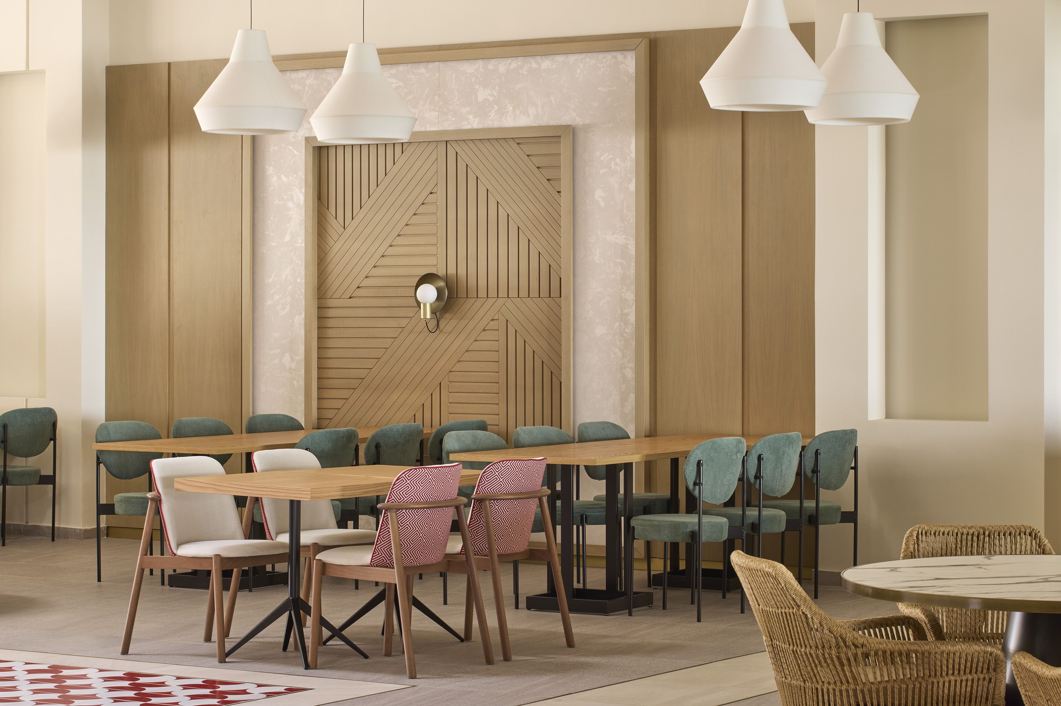 A modern dining area with a long wooden table, green upholstered chairs, and white pendant lights.