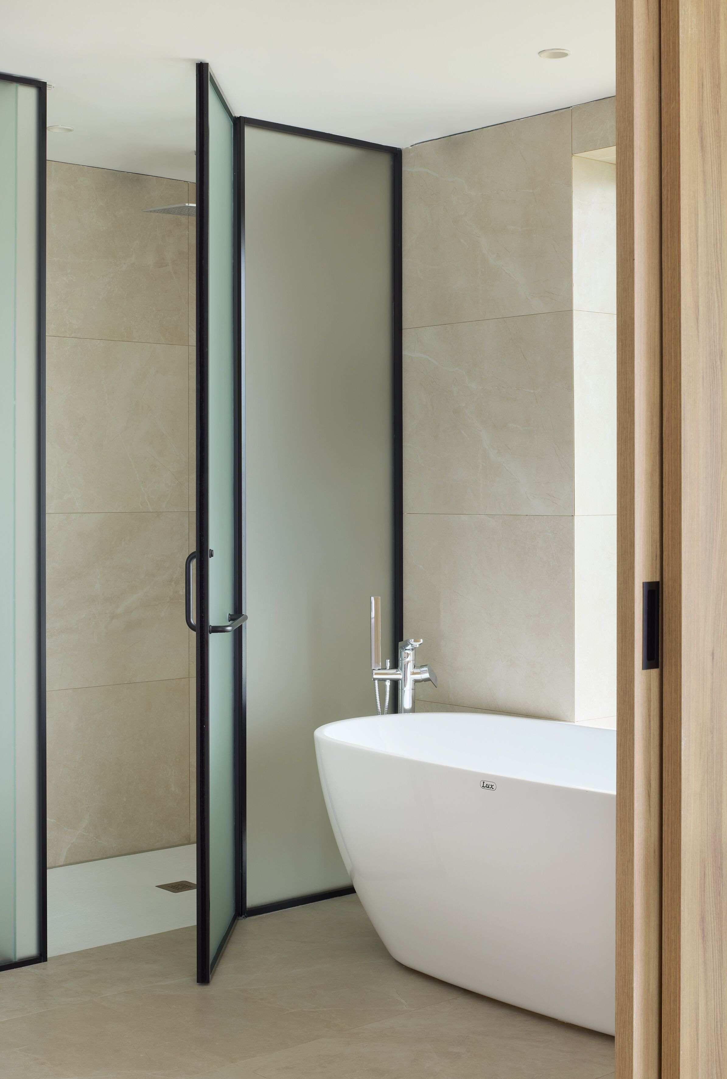 Un baño moderno con una bañera independiente, una cabina de ducha con mampara de vidrio y una puerta de madera.