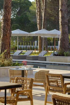 A poolside area with wicker chairs, a table, and umbrellas. - Melia Durres Albania (Ishëm)