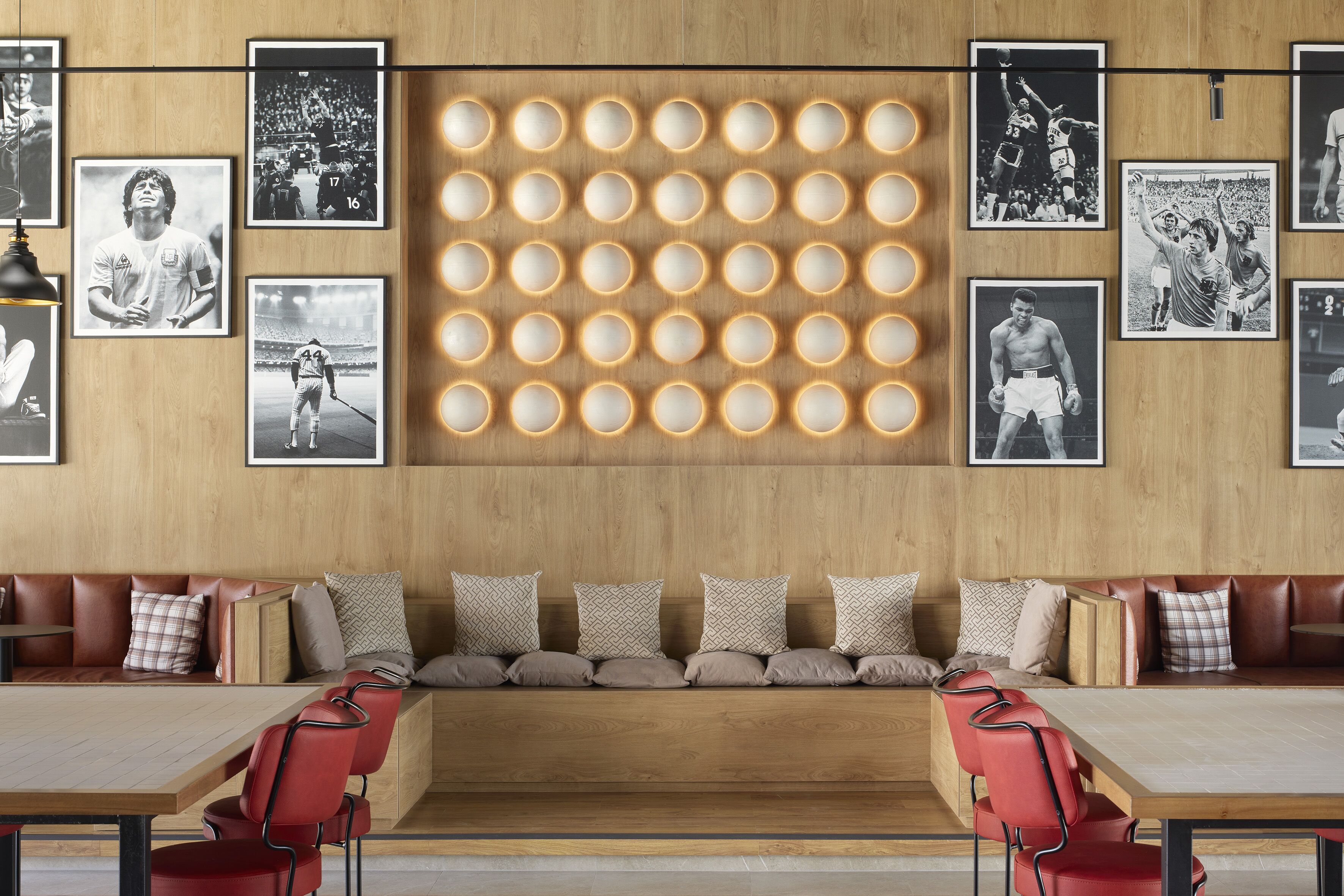 A modern restaurant with a long communal table, cushioned seating, and framed sports photographs on the walls.