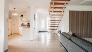 Ein modernes Wohnzimmer mit einer Couch, einer Holztreppe und einer Küchenzeile im Hintergrund.