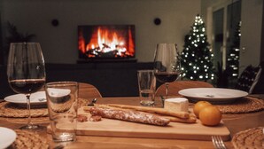 Ein Esstisch ist gedeckt mit Tellern, Gläsern und verschiedenen Speisen, im Hintergrund ein Kamin und ein Weihnachtsbaum.