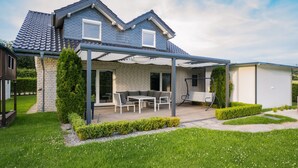Ein Haus mit überdachter Terrasse, Backsteinfassade und gepflegtem Rasen.