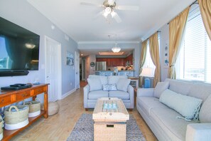 A living room with a sofa, a coffee table, a television, and a kitchen in the background.