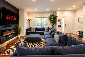 A modern living room with a sectional sofa, a flat-screen TV, a fireplace, and a large window.