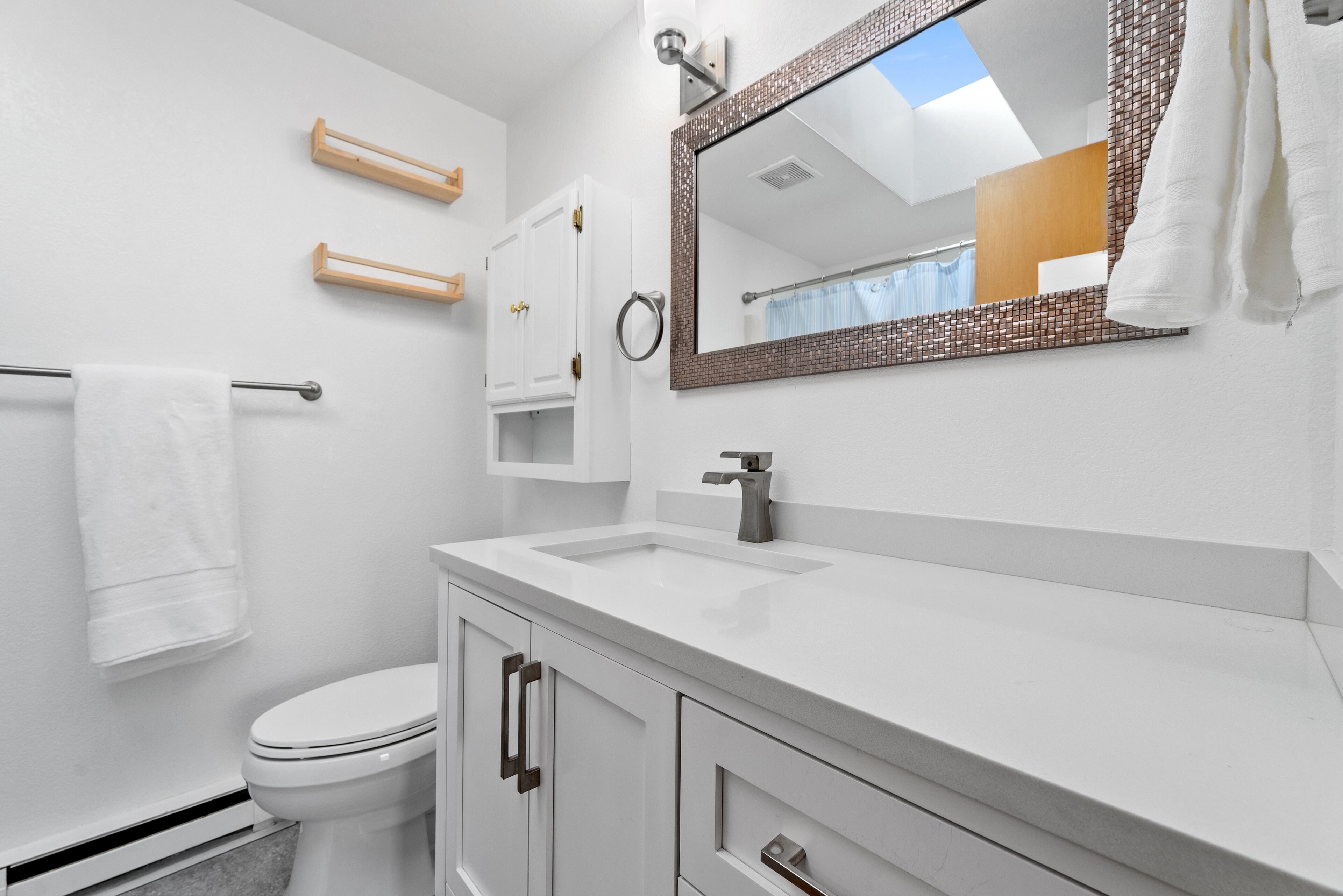 A modern bathroom with a white sink, a mirror with a decorative frame, and a toilet.