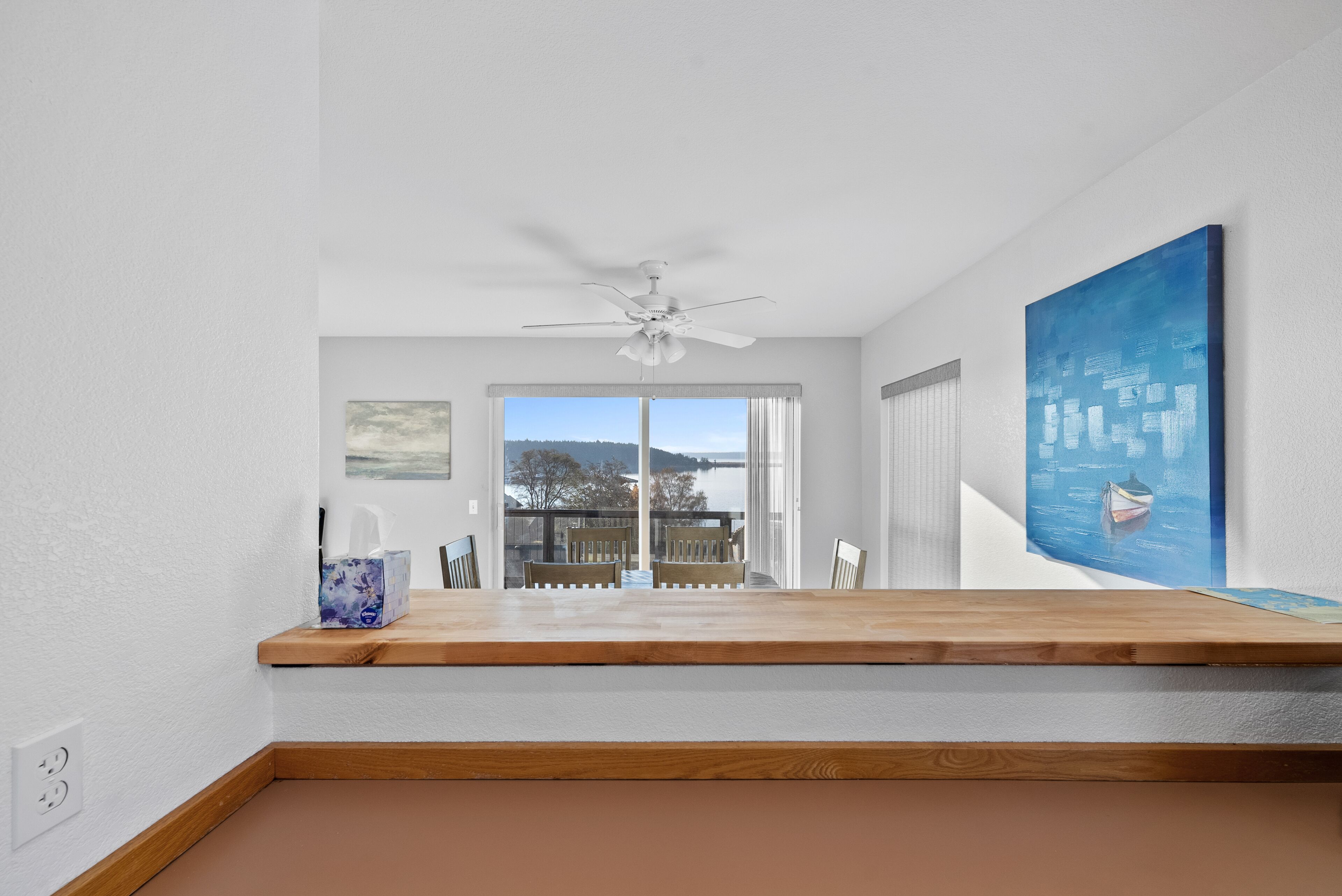 Quarto moderno com mesa de madeira, ventilador de teto, quadro e vista para o exterior.