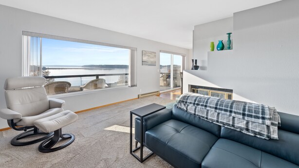 Een moderne woonkamer met uitzicht op zee, een relaxfauteuil, een donkerblauwe bank en een kleine tafel.
