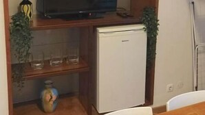 Ein kompakter Wohnbereich mit Fernseher auf einem Regal, einer kleinen Kühlmöglichkeit und einem Esstisch.