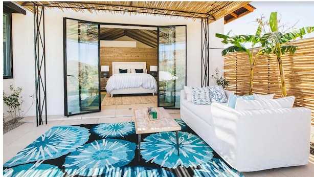 A modern bedroom with a large bed, a white sofa, and a glass door leading to a balcony.