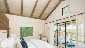 A bedroom with a bed, a nightstand, a window with curtains, and a view of an outdoor area.