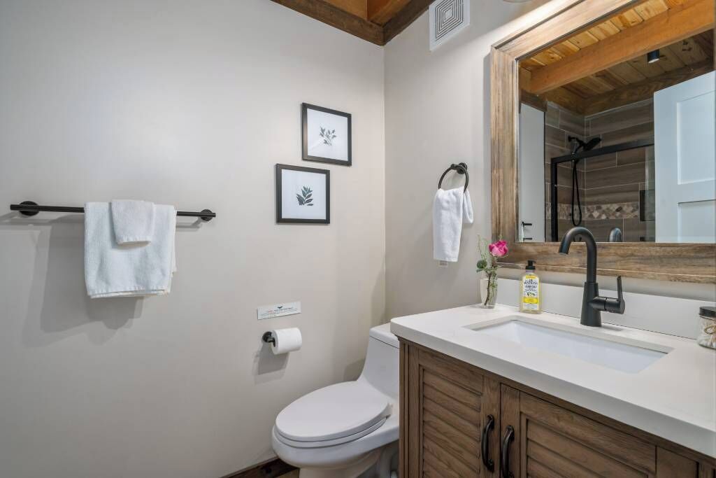 A bathroom with a white toilet, a sink with a wooden cabinet, a mirror, and two framed pictures on the wall.