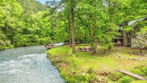 A riverside property with a wooden deck, a stone pathway, and a building with a sloped roof. - The Grande Lodge- Riverfront, Fiber, HotTub, Fish, DogOK, Game Room, Movie Room (Ellijay)