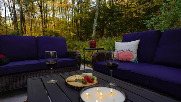 An outdoor seating area with two purple sofas, a table with a candle, wine glasses, and a plate of food. - Woodlands Retreat (Lake George)