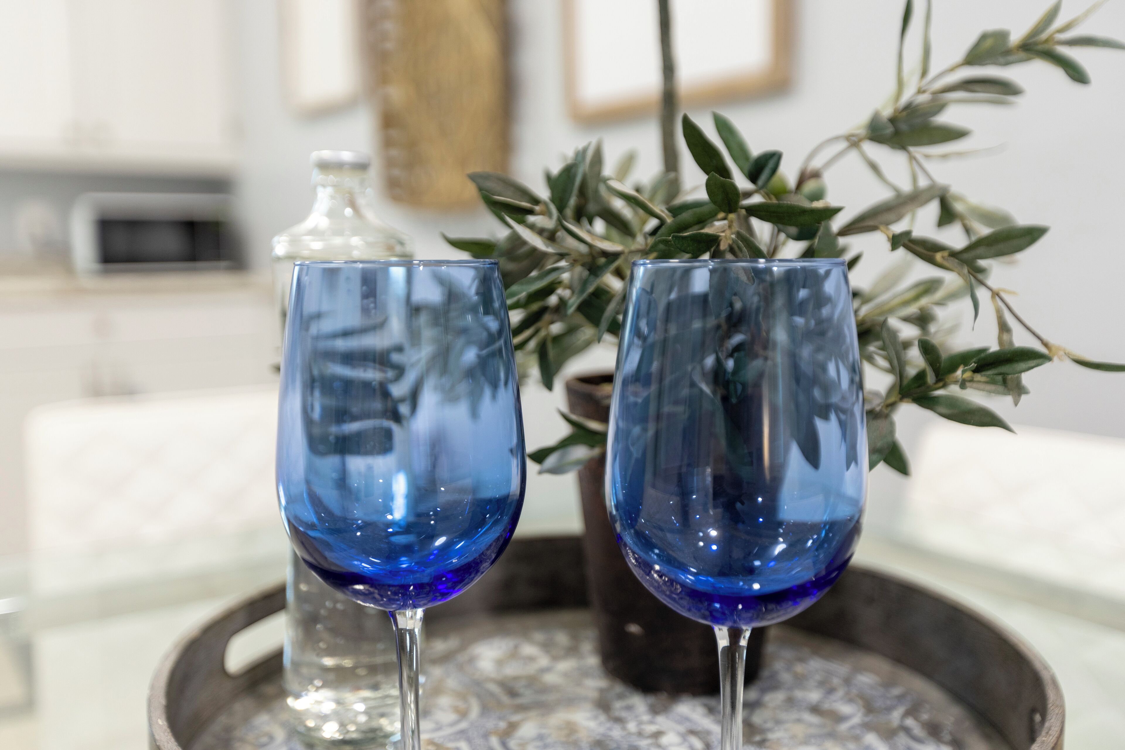 Two blue glass wine glasses on a tray with a decorative centerpiece.