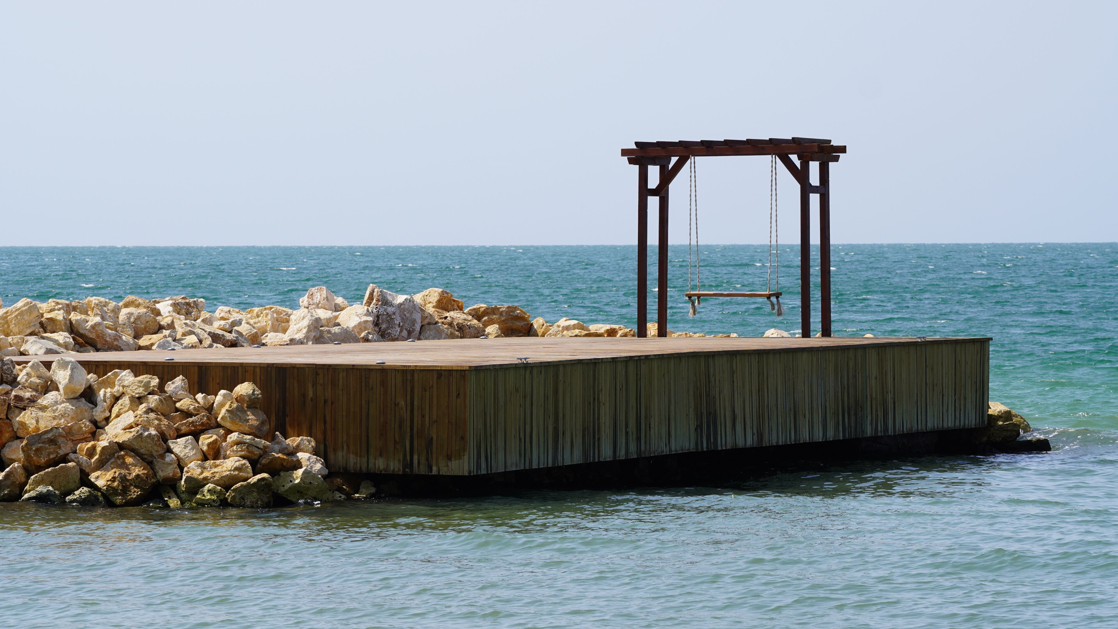 Une jetée en bois s’étendant dans des eaux calmes, avec une balançoire en bois et un petit abri.