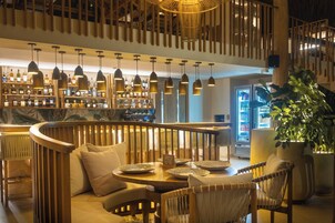 Zona de bar con mobiliario de madera, lámparas colgantes y estantes llenos de botellas.