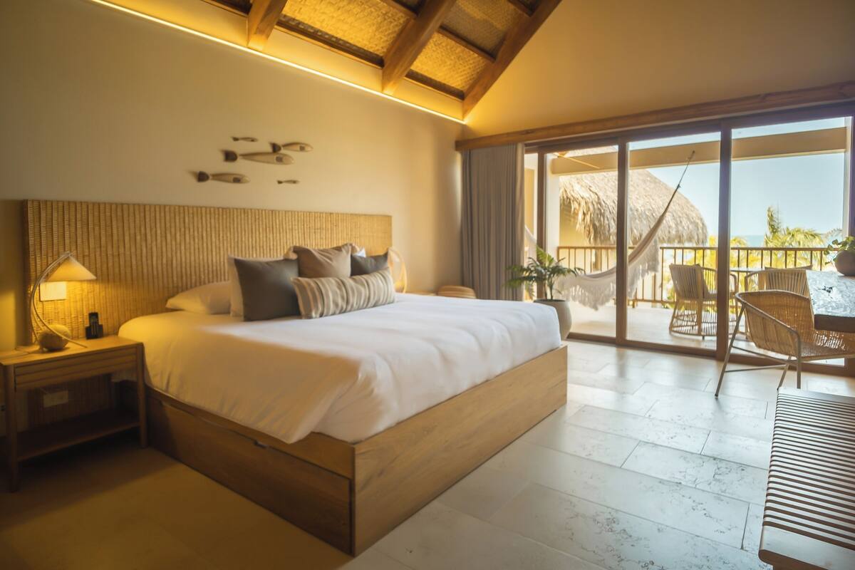 A spacious bedroom with a large bed, wooden headboard, and a view of the balcony.