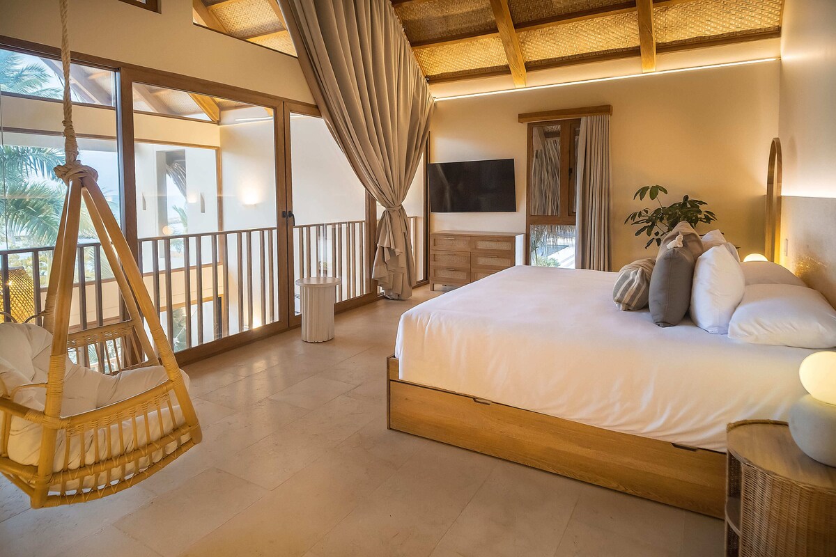 A bedroom with a bed, hanging chair, TV, and large windows.
