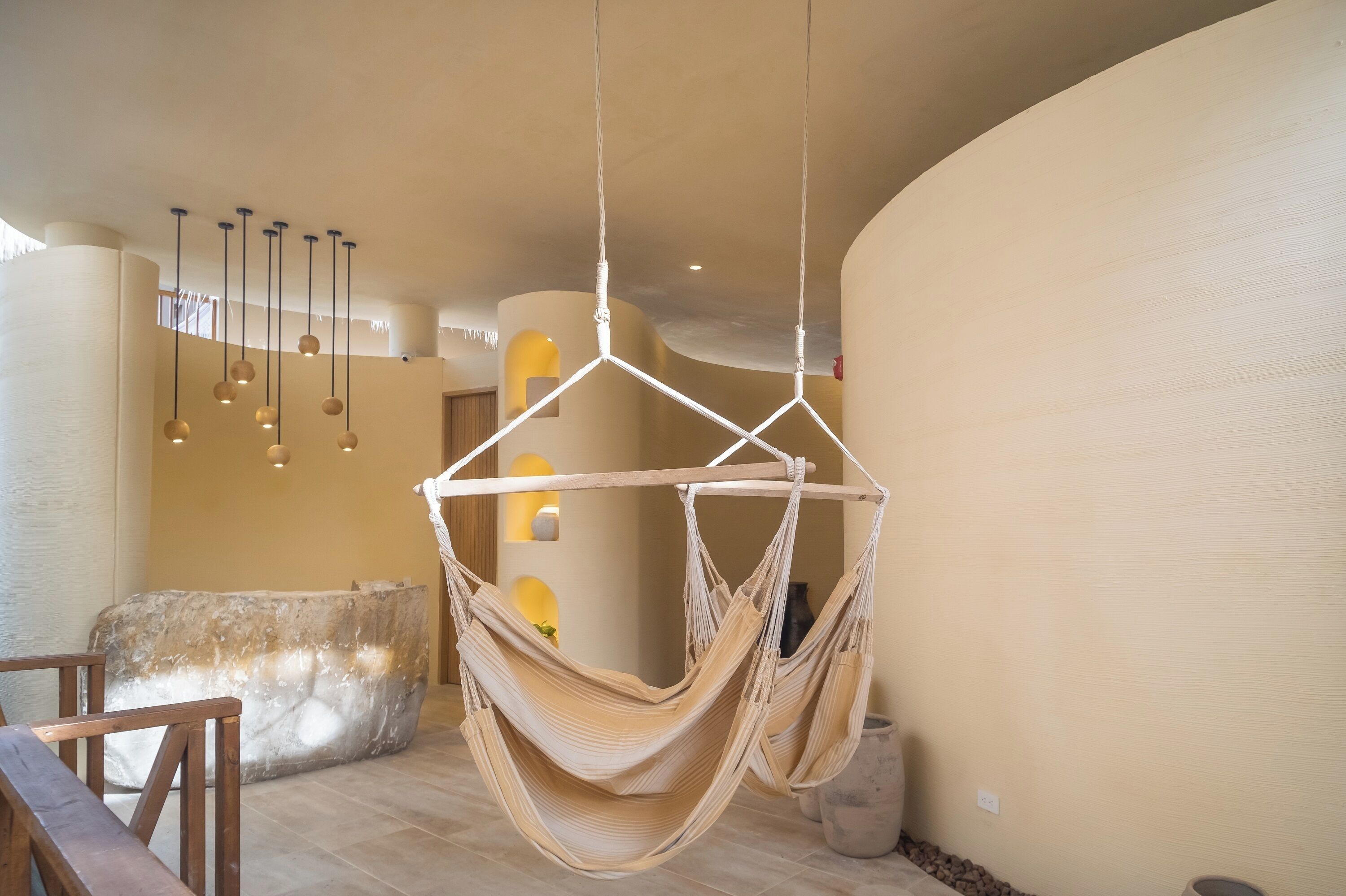 A hammock chair suspended from the ceiling in a room with a stone bench and a wooden table.