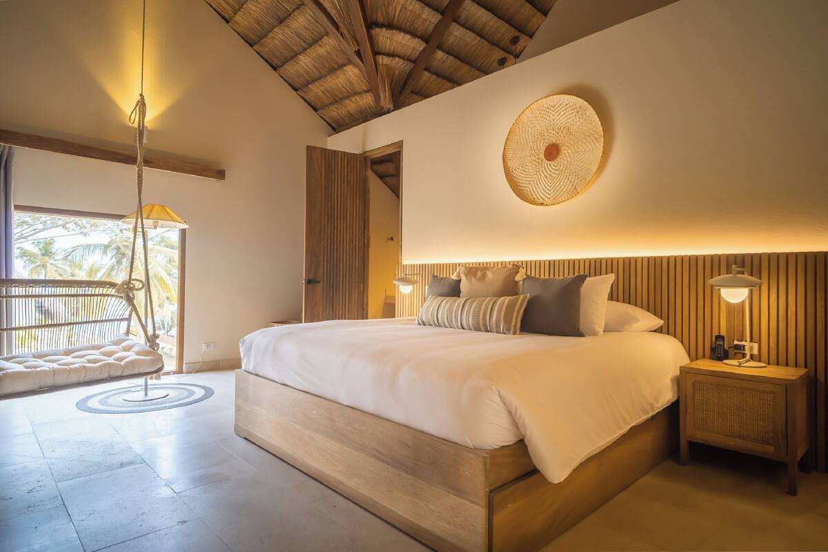 A spacious bedroom with a large bed, a hanging chair, and a bedside table with a lamp.