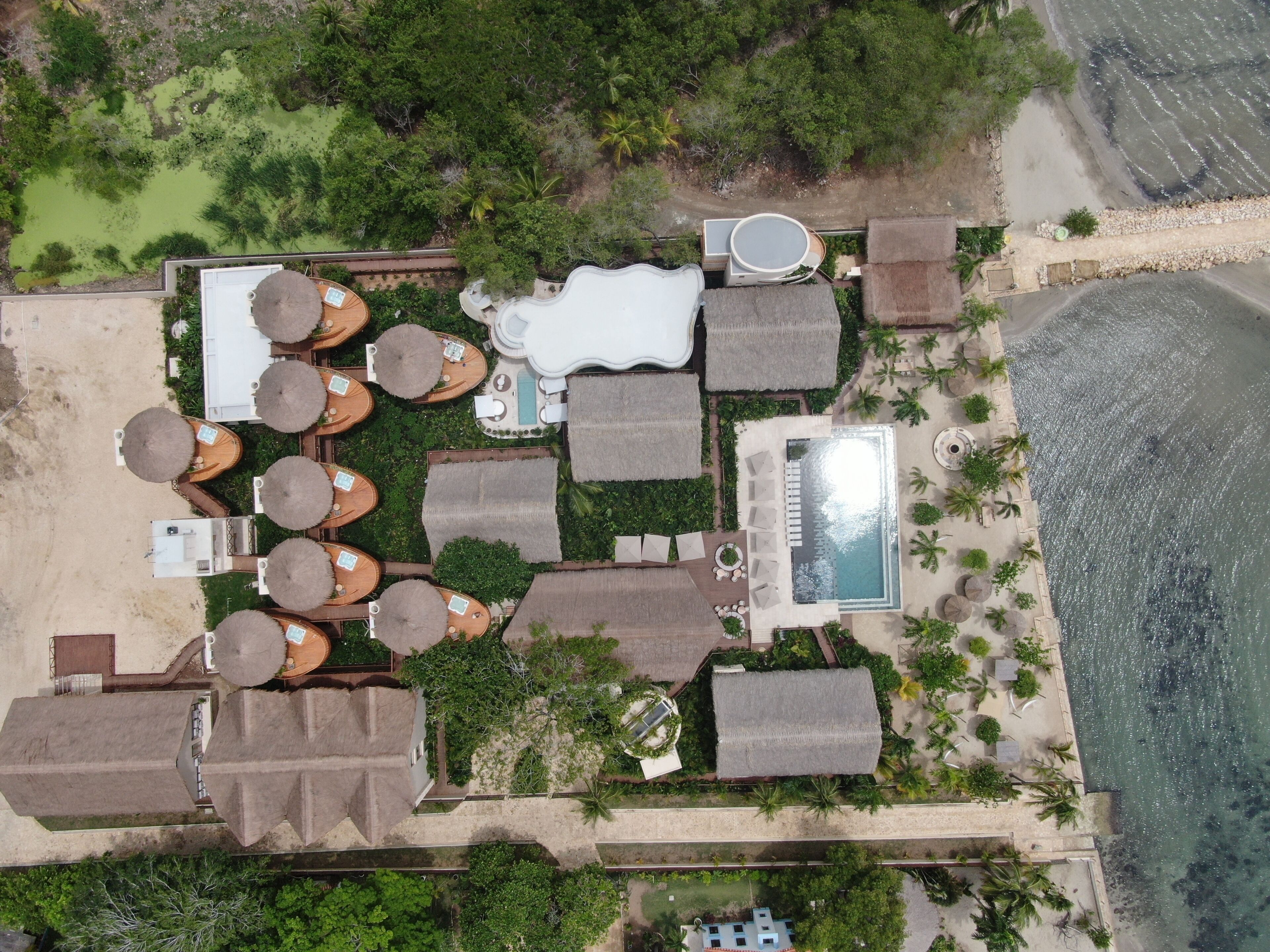 An aerial view of a resort with multiple bungalow-style accommodations, a swimming pool, and a beachfront.