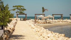 A beach with a stone wall, lounge chairs, umbrellas, and a clear view of the sea. - Hotel Aimarawa (San Antero)