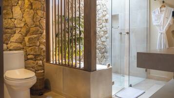 A bathroom with a stone wall, a glass shower enclosure, and a white bathtub.
