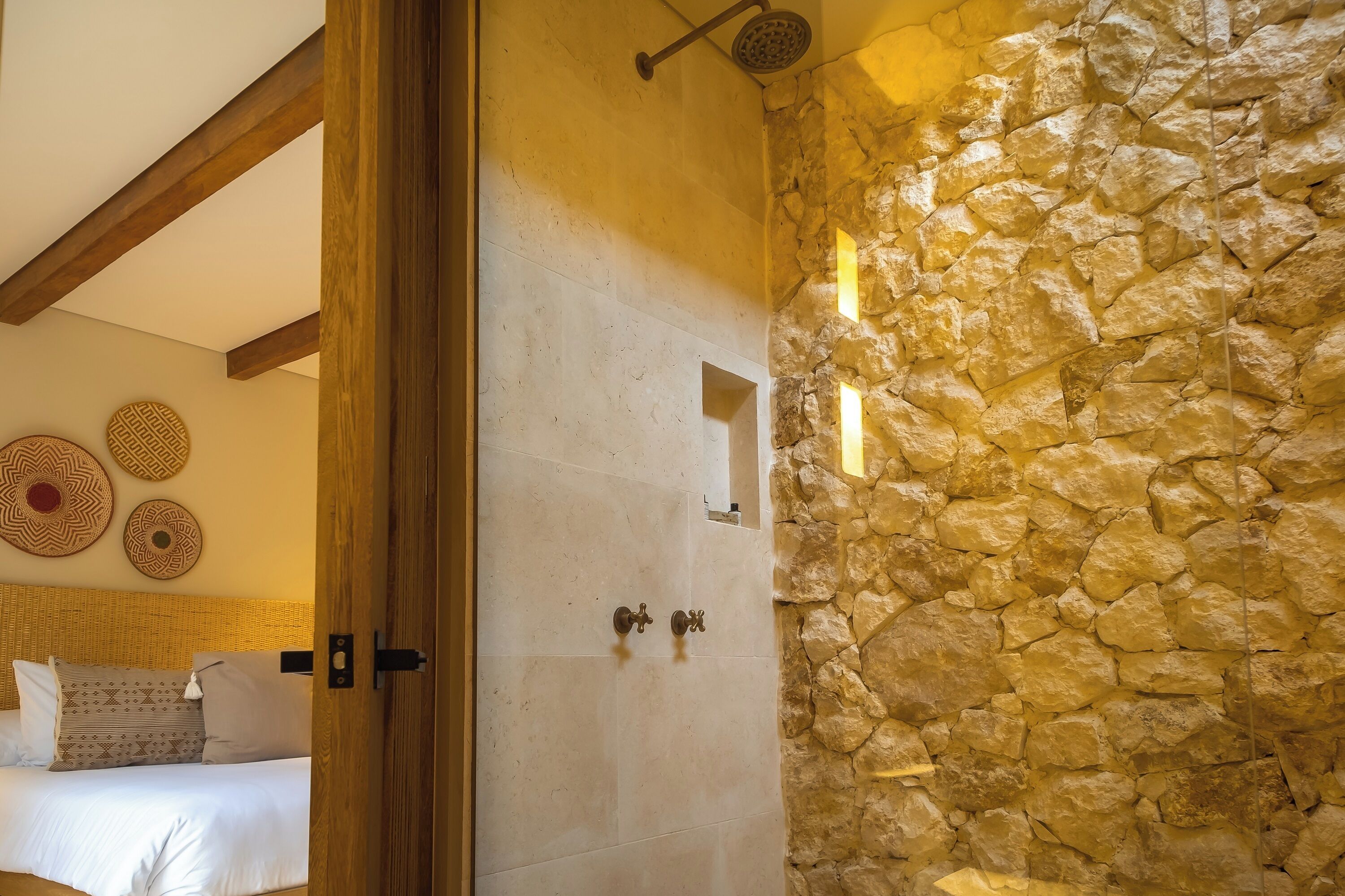 Un dormitorio con pared de piedra, una cama con almohadones estampados y una viga de techo de madera.