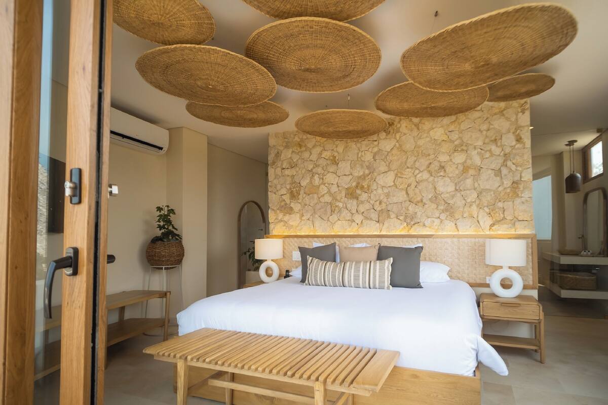 A bedroom with a stone wall, a bed with white bedding, two bedside tables, and a wooden bench.