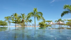 A clear blue pool surrounded by palm trees and beach huts. - Hotel Aimarawa (San Antero)