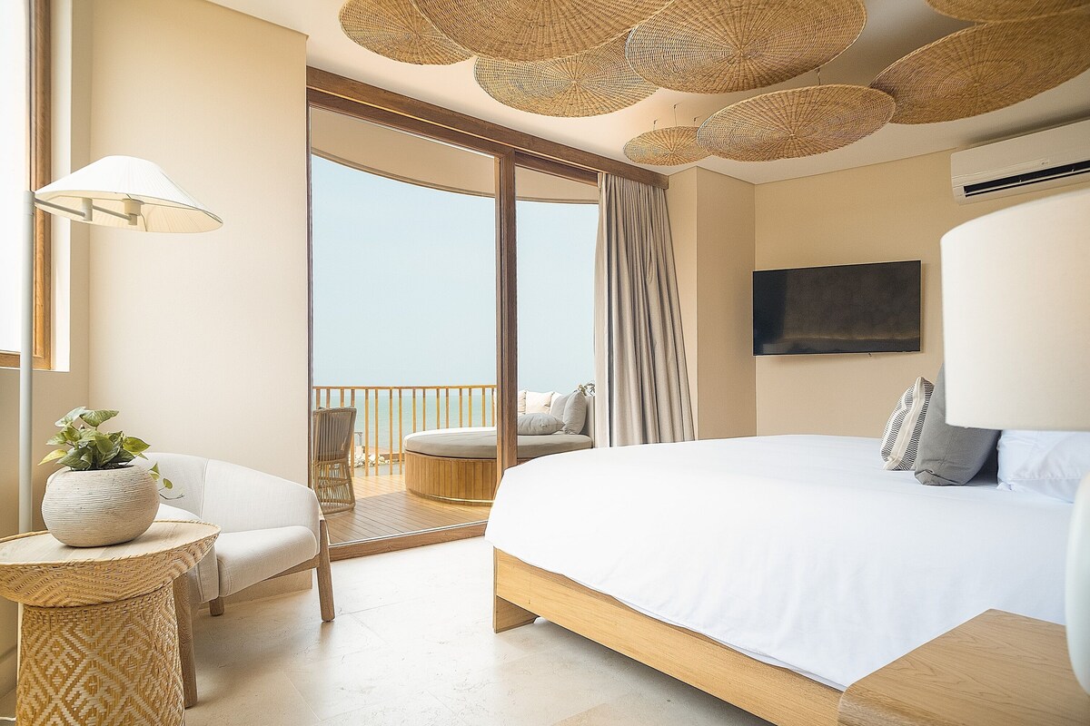 A modern bedroom with a large bed, a balcony with a view, and a television on the wall.