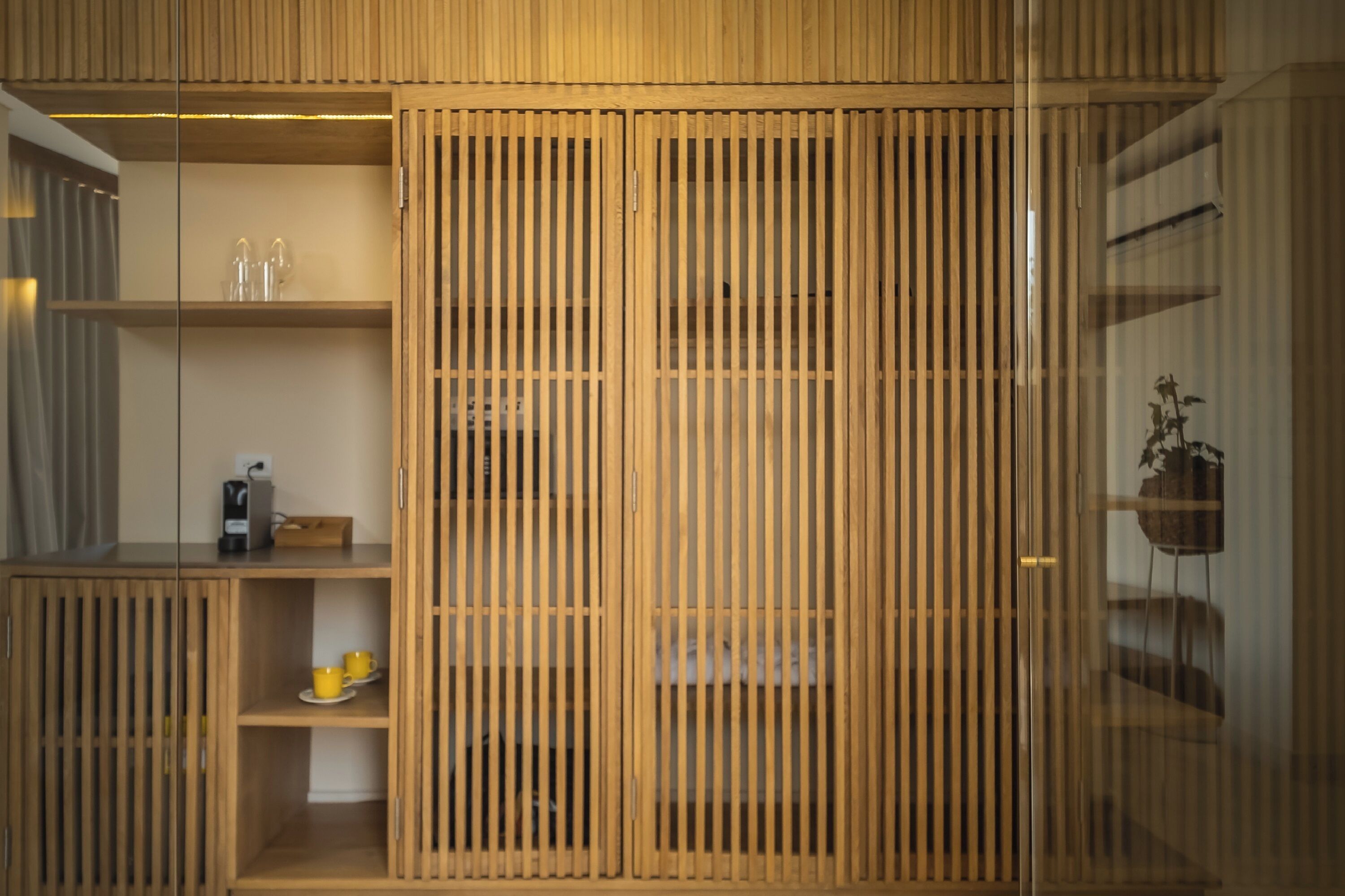 A room with a sliding wooden partition, a shelf with cups, a kettle, and a small plant.
