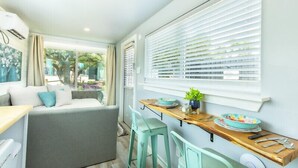 A modern kitchen with a grey sofa, teal chairs, and a wooden table with a bowl of fruit.