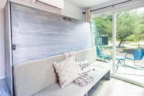 Quarto com uma grande porta de vidro deslizante que dá para uma área externa com cadeiras azuis e uma pequena mesa.