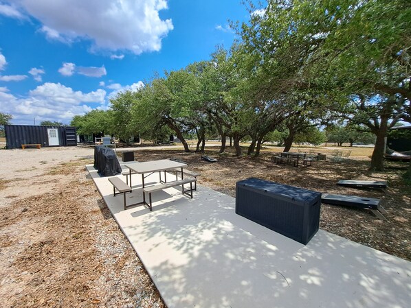 Un patio al aire libre con una mesa de picnic y bancos, rodeado de árboles y cielo despejado.