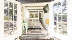 Un dormitorio con cama, televisor montado en la pared y vistas al exterior a través de amplias ventanas.