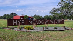 Señal de la bodega Hye Meadow, con un campo cubierto de hierba y árboles al fondo.