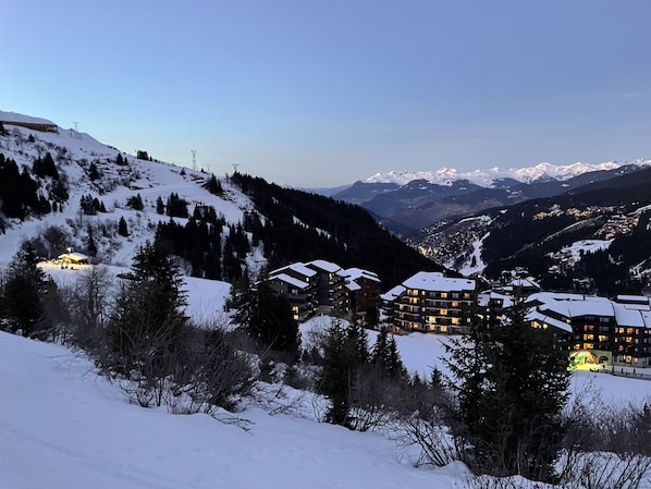 A snow-covered mountain resort with multiple buildings, including a lodge with balconies and a ski slope in the background.